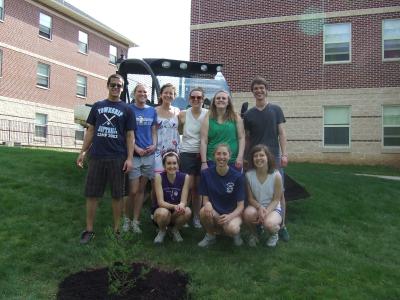 philosophy students standing by tree they planted with bulldozer behind them