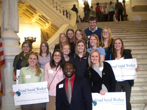group of social work students on steps inside capitol holding proud social worker signs