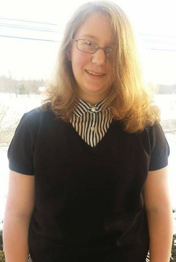 Mk is facing the camera smiling while wearing a black top with a striped shirt underneath